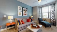 This thoughtfully designed single-floor residence offers a cohesive blend of color, comfort, and functionality across its well-organized layout. The living room serves as the heart of the home, featuring a striking blue accent wall adorned with eclectic artwork, plush carpeting, and a large window dressed in bold patterned curtains that invite ample natural light. A chaise lounge positioned near the window creates a cozy reading nook within the space.

The galley-style kitchen is equipped with dark countertops, light wood cabinetry, a black electric range, and rich wood-look flooring that extends seamlessly into the hallway. A dedicated in-unit laundry room is conveniently accessible directly from the kitchen corridor.

Two well-proportioned bedrooms each carry their own distinct character — one features warm neutral tones with direct access to an outdoor balcony, while the other showcases a bold olive green accent wall paired with carpeted flooring and generous natural light from a large window. Both bedrooms include closet storage, with at least one walk-in closet offering built-in shelving.

The two bathrooms are finished with wood-look flooring, clean white fixtures, and tiled tub-shower combinations. An en-suite bathroom off the primary bedroom features a spacious vanity with ample counter space. Throughout, the residence balances vibrant design accents with practical, comfortable living.