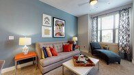 This thoughtfully designed single-floor residence offers a cohesive blend of color, comfort, and functionality across its well-organized layout. The living room serves as the heart of the home, featuring a striking blue accent wall adorned with eclectic artwork, plush carpeting, and a large window dressed in bold patterned curtains that invite ample natural light. A chaise lounge positioned near the window creates a cozy reading nook within the space.

The galley-style kitchen is equipped with dark countertops, light wood cabinetry, a black electric range, and rich wood-look flooring that extends seamlessly into the hallway. A dedicated in-unit laundry room is conveniently accessible directly from the kitchen corridor.

Two well-proportioned bedrooms each carry their own distinct character — one features warm neutral tones with direct access to an outdoor balcony, while the other showcases a bold olive green accent wall paired with carpeted flooring and generous natural light from a large window. Both bedrooms include closet storage, with at least one walk-in closet offering built-in shelving.

The two bathrooms are finished with wood-look flooring, clean white fixtures, and tiled tub-shower combinations. An en-suite bathroom off the primary bedroom features a spacious vanity with ample counter space. Throughout, the residence balances vibrant design accents with practical, comfortable living.