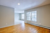 Located at 127 Spring Ave in Watertown, NY, this 2-bedroom, 2-bathroom apartment offers a practical and comfortable single-floor layout. The entryway opens to light-colored tile flooring that transitions into warm hardwood floors in the main living area, which features large windows that invite generous natural light and views of the surrounding neighborhood. Baseboard heating is present throughout the unit, ensuring consistent warmth year-round.

The kitchen is well-appointed with honey-toned oak cabinetry, granite-patterned countertops, a double stainless steel sink, and a full range with overhead ventilation. Tile flooring continues through this space, making it easy to maintain.

Both bedrooms are carpeted and finished in neutral tones, offering a quiet, comfortable atmosphere. The primary bedroom provides a comfortable footprint with a built-in closet featuring double bi-fold doors. The second bedroom includes a large window with exterior views and baseboard heating. Each bedroom benefits from soft, plush carpeting.

The full bathroom includes an oak vanity with a white countertop, tile flooring, and a full tub-shower combination. A second half-bath is also available. A connecting hallway links all rooms efficiently, contributing to the unit's functional and straightforward floor plan.
