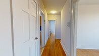 Located at 33 Coleman Street in Bridgeport, CT, this single-floor residence offers three bedrooms, one bathroom, a kitchen, and a hallway, all tied together by warm hardwood flooring that runs throughout the space. The layout is efficiently organized, with a central hallway connecting the rooms and fitted with classic paneled white doors and flush ceiling lighting.

The spacious primary bedroom is the largest of the three, featuring multiple windows that invite generous natural light and offer views of the surrounding Bridgeport neighborhood, including a glimpse of a nearby church steeple. Classic cast-iron radiators are present in the bedrooms, providing character alongside practical heating. The additional bedrooms are bright and well-proportioned, each with their own windows and clean white walls.

The galley-style kitchen is outfitted with warm honey-toned wood cabinetry, granite-look countertops, and black appliances including a refrigerator and range. A window and glass-panel door in the kitchen bring in natural light and exterior views. The bathroom features white subway tile surrounding the tub-shower combo, mosaic floor tiling, a window for ventilation, and a granite-topped vanity area, maintaining a clean and functional aesthetic throughout.