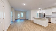 This well-appointed single-story home in Charlotte, NC offers three bedrooms and two bathrooms within a thoughtfully designed floor plan. The open-concept kitchen and living area serves as the heart of the home, featuring light luxury vinyl plank flooring that flows throughout the main spaces. The kitchen is outfitted with crisp white shaker cabinets, granite countertops, a central island with pendant lighting, and a full suite of stainless steel appliances, including a refrigerator, range, and built-in microwave. A door off the living area leads to a private balcony, bringing in natural light and outdoor views through multiple windows.

The bedrooms offer plush carpeting and generous proportions, with the primary bedroom accompanied by an en-suite bathroom complete with a glass-enclosed shower, wood-look flooring, a granite-topped vanity, and a spacious walk-in closet outfitted with wire shelving systems. Secondary bedrooms feature double-door closets and windows overlooking lush greenery. A dedicated laundry room houses a full-size washer and dryer with overhead shelving for added storage. Clean white walls, consistent finishes, and a bright, neutral palette give the entire home a modern, move-in-ready feel.