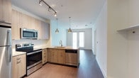This well-appointed 1-bedroom, 1-bathroom residence offers a thoughtfully designed open-concept floor plan that seamlessly connects the kitchen and living areas. The modern kitchen serves as the heart of the home, featuring light wood cabinetry, a subway tile backsplash, and a peninsula island with an undermount sink and pendant lighting overhead. Stainless steel appliances — including a dishwasher, electric range, and built-in microwave — provide both style and functionality. Track lighting above the kitchen adds a contemporary touch and ensures excellent task illumination. Rich, dark hardwood-style flooring runs throughout, creating a warm contrast against the crisp white walls. The living area is generously proportioned, bathed in natural light streaming through glass-paneled doors that lead to a private balcony, offering an inviting indoor-outdoor connection. Clean architectural lines, neutral tones, and an efficient single-floor layout make this unit a practical yet stylish living space suited for modern everyday living.