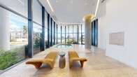 This single-level spa and wellness facility is designed with a refined, resort-inspired aesthetic that balances openness with intimate comfort. The centerpiece of the space is a luminous indoor pool area enclosed by expansive floor-to-ceiling glass walls, flooding the room with natural light and offering unobstructed views of surrounding tropical greenery. Soaring ceilings, a sculptural concrete column with a warm gold-toned cap detail, and a mosaic-tiled floor beneath woven lounge chairs create a serene, gallery-like atmosphere. Recessed linear lighting traces the ceiling perimeter, adding a soft, contemporary glow throughout.

Adjacent to the pool lounge, a dedicated infrared sauna room is finished entirely in warm cedar wood paneling, with built-in infrared heating panels and recessed ceiling lighting, offering a private retreat for therapeutic use. A door with navy steel-framed glazing connects the spa to an outdoor fitness area. Hallways leading through the facility are adorned with curated artwork, including nautical-themed photography and fine art paintings, reinforcing a sophisticated, gallery-quality ambiance. A posted spa rules placard and clearly defined entry and exit points reflect the facility's well-organized, professional layout throughout.
