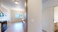 This single-floor unit offers a clean, contemporary design with a bright and functional layout. Light wood-tone laminate flooring runs consistently throughout the space, creating a cohesive and warm aesthetic. The entry welcomes with a glass-paneled front door flanked by sidelight windows, filling the foyer with natural light.

The galley-style kitchen is well-appointed with light wood cabinetry featuring sleek black hardware, white countertops, a stainless steel sink, and black appliances including a refrigerator, electric range, and built-in microwave. Ample upper and lower cabinet storage is complemented by a louvered closet door leading to additional storage beyond.

The living and dining areas are open and spacious, with a pendant chandelier adding an elegant touch above the dining space. A large window provides views to the exterior and draws in natural light.

The bedrooms are generously sized with neutral wall tones, large windows with blinds, and light flooring. One bedroom features a ceiling fan with light fixture and a wall-mounted HVAC unit for individual climate control.

The bathroom is thoughtfully finished with decorative patterned floor tile, a wood-toned vanity with white countertop, a large mirror, and a full soaking tub with shower combination. The space is clean and modern throughout, offering a comfortable and move-in-ready environment.