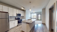 This single-floor residence offers a thoughtfully designed open-concept layout that seamlessly connects the kitchen and living areas. The kitchen is a standout feature, showcasing crisp white cabinetry, granite countertops, a classic subway tile backsplash, and a full suite of stainless steel appliances including a refrigerator, range, and microwave. A central island with an integrated sink and pendant lighting above serves as both a functional workspace and a natural gathering point. Wood-look hard flooring extends throughout the kitchen and main living areas, transitioning to plush carpeting in the bedroom and living room. Natural light flows generously through large windows, brightening the open living space, which also features a ceiling fan for added comfort. The bedroom is well-sized with its own window and direct access to a spacious walk-in closet outfitted with wire shelving and hanging rods on multiple walls for ample storage. The bathroom is finished with granite-topped vanity cabinetry, a framed mirror, and wood-look flooring that continues the cohesive aesthetic throughout. The overall ambiance is clean, contemporary, and move-in ready, with neutral tones and modern fixtures creating a bright and inviting atmosphere throughout.