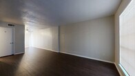 This two-story home offers a functional and well-organized layout spread across two floors of comparable size. The main level features a combined kitchen and living room area finished with rich, dark hardwood-style flooring that extends throughout, creating a cohesive and grounded aesthetic. The living room is open and airy, benefiting from natural light through large windows dressed with vertical blinds, and is equipped with a ceiling fan. The kitchen includes light-toned countertops and black appliances, complementing the neutral wall palette found throughout the home. A staircase connects the main floor to the upper level, where three bedrooms and two bathrooms are located. The primary bedroom offers a comfortable footprint with carpeted flooring, a ceiling fan, and a window providing natural light. The additional bedrooms are similarly carpeted and feature ceiling fans, lending a consistent, practical finish. The two bathrooms are clean and simply appointed, with light cabinetry and speckled countertops. A hallway and closet round out the upper floor's layout. Throughout the home, neutral gray and beige tones create a calm, understated atmosphere well-suited for a variety of living arrangements.