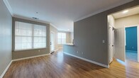 This single-floor unit offers a thoughtfully designed layout that balances open communal spaces with functional private areas. The living and dining areas flow seamlessly together, finished with warm hardwood-style flooring and neutral gray walls accented by crisp white crown molding and baseboards. Multiple windows fitted with blinds allow natural light to fill these spaces, enhancing the clean, contemporary aesthetic. A pass-through peninsula connects the main living area to the kitchen, providing both visual openness and practical utility.

The kitchen is well-equipped, featuring white shaker-style cabinetry with matte black hardware, a marble-patterned tile backsplash, light wood flooring, and a full suite of stainless steel appliances including a gas range, over-the-range microwave, and refrigerator. Ample upper and lower cabinet storage adds to the kitchen's functionality.

The bedroom is a generously sized, carpeted room with windows on two walls, offering abundant natural light and a comfortable, quiet atmosphere. The bathroom includes a full tub-shower combination with white tile surround, chrome fixtures, grab bars, and wood-style flooring, reflecting a practical and accessible design. Overall, the space maintains a consistent, modern palette throughout.