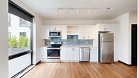 Located at 3737 Farnam St. in Omaha, Nebraska, this modern two-bedroom, one-bathroom unit offers a thoughtfully designed layout with clean, contemporary finishes throughout. Warm hardwood flooring flows seamlessly across the open living area, kitchen, hallway, and both bedrooms, creating a cohesive and inviting aesthetic.

The kitchen is a standout feature, equipped with stainless steel appliances including a range, microwave, dishwasher, and refrigerator. Crisp white cabinetry extends to the ceiling, complemented by a blue-gray subway tile backsplash and track lighting overhead, balancing function with modern style.

The primary bedroom is a comfortable retreat, highlighted by a dramatic floor-to-ceiling window with black-framed trim that fills the room with natural light and frames views of the surrounding Omaha neighborhood. The second bedroom also features large black-framed windows with roller shades, offering similar city views and abundant daylight.

The full bathroom is finished with large-format gray tile flooring, a white vanity with an integrated sink and round mirror, and a full tub-shower combination. Bold black door frames and trim accent the clean white walls throughout the unit, lending a sharp, modern edge. A central hallway connects the bedrooms and bathroom, providing an efficient and functional flow through the entire space.