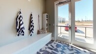 This single-floor pet spa is a thoughtfully designed facility built entirely around the needs of dogs and their owners. The space makes an immediate impression with its bold, dog-silhouette wallpaper adorning the upper walls of the wash area, set against crisp white subway tile that lines the sides of two generously sized, walk-up dog bathing stations. Each station features a raised platform with a center drain and a handheld showerhead with adjustable fixtures, making bath time efficient and comfortable for pets of all sizes. Large windows flood the wash area with natural light and offer views of the surrounding exterior. The geometric-patterned tile flooring — a striking monochromatic design in shades of grey, white, and charcoal — runs throughout the space, adding a modern, polished aesthetic. Adjacent to the wash stations is a dedicated grooming area equipped with a professional grooming table, a wall-mounted mini-split climate control unit, and a decorative framed artwork piece that softens the utilitarian elements. A well-appointed mudroom entry completes the layout, featuring wall-mounted hooks for leashes and towels, a built-in bench, a compact open shelving unit for supplies, and a glass exterior door that connects directly to the outdoors — making post-walk cleanup seamless and organized.