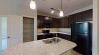 Located at 56 Bent Branch Loop in Clayton, NC, this single-story home offers a thoughtfully designed layout with functional living spaces throughout. The kitchen is a standout feature, showcasing rich dark-espresso cabinetry extending to the ceiling, speckled granite countertops, black appliances including a range, microwave, and refrigerator, and a large island with a double stainless steel sink. Pendant lighting and a dedicated pantry with wire shelving add both style and practicality to the space. The open living area is bright and welcoming, with plush carpet underfoot, a ceiling fan, and multiple windows fitted with blinds that invite natural light. The primary bedroom is generously proportioned with a tray ceiling, natural light from a window, and direct access to both a private bathroom and a sizable walk-in closet with wire shelving. Additional bedrooms are carpeted and well-sized. Bathrooms feature tub-shower combinations with white surrounds, wood-look flooring, and granite-topped vanities. A dedicated laundry area houses a full-size side-by-side washer and dryer. Throughout the home, neutral tones, clean finishes, and consistent design elements create a cohesive and comfortable living environment.
