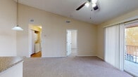 This single-story unit is thoughtfully laid out to maximize functionality across its living spaces. The main living area is generously proportioned, featuring vaulted ceilings, neutral-toned carpet, and a ceiling fan with integrated lighting. A pass-through peninsula connects the living space to the kitchen, creating an open, airy feel. The front entry door opens directly into this shared living zone, enhancing accessibility.

The galley-style kitchen is equipped with warm-toned wood cabinetry extending to the upper walls, granite-look countertops, a double basin sink, and white appliances including a refrigerator, electric range, dishwasher, and built-in microwave. Light hardwood-style flooring runs throughout the kitchen and extends into the bathroom and laundry areas.

The bathroom features a tiled shower-tub combination, a wood vanity with granite-look countertop, a single sink, and a large mirror. A dedicated laundry area accommodates a full-size washer and dryer.

Both bedrooms are carpeted and include ceiling fans with lighting. One bedroom offers a sliding glass door leading to a private balcony with outdoor views, while the other features a window with natural light and a closet. The overall ambiance is clean, neutral, and move-in ready.