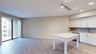 This 1-bedroom, 1-bathroom corner unit at Mayala in Pompano Beach, Florida offers a thoughtfully designed, open-concept layout finished with consistent wood-look tile flooring throughout. The living and dining area is bright and airy, featuring neutral warm-toned walls, clean white baseboards, and track lighting that enhances the open feel of the space. Sliding glass doors lead to a private balcony with views of the surrounding community.

The kitchen is well-appointed with crisp white shaker-style cabinetry extending to the ceiling, providing ample storage. A gray subway tile backsplash adds a modern touch, while stainless steel appliances — including a refrigerator, range, microwave, and dishwasher — offer full functionality. A white kitchen island serves as both a prep surface and casual dining area.

The bedroom is generously sized and includes its own sliding glass door access to the balcony, filling the room with natural light. A spacious walk-in closet with built-in shelving and hanging rods provides excellent storage capacity.

The bathroom features a white vanity with quartz-style countertop, an illuminated LED mirror, and a full soaking tub with tiled surround, all finished in a clean, contemporary palette that ties the unit together cohesively.