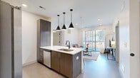 This thoughtfully designed 2-bedroom, 2-bathroom residence at 2005 Brook Rd in Richmond, VA offers a contemporary living experience across a single floor. The open-concept kitchen and living area forms the heart of the space, where dark wood-grain cabinetry, crisp white quartz countertops, and a central island with an undermount sink create a functional yet stylish kitchen. A suite of stainless steel appliances, including a French door refrigerator, electric range, and built-in microwave, rounds out the modern kitchen. Three matte black pendant lights hang above the island, adding a striking design element. The living room flows seamlessly from the kitchen and is bathed in natural light from a full-width sliding glass door that opens to a private outdoor balcony. The primary bedroom is generously proportioned, featuring plush carpet, direct access to a dedicated bathroom, and a closet. The second bedroom offers a comfortable, well-lit retreat. Both bathrooms are finished with modern floating vanities, white quartz counters, and dark wood cabinetry. A hallway and two closets provide practical storage throughout. Recessed lighting and clean white walls lend a bright, cohesive ambiance throughout the entire residence.