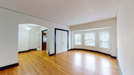 This single-floor unit showcases a consistent design language throughout, highlighted by warm hardwood flooring that runs seamlessly across every room. Bold navy blue door and window trim contrasts sharply against white walls, lending the space a distinctive, classic character.

The expansive living area is a standout feature, defined by a graceful curved bay window that floods the room with natural light. An elegant arched doorway connects the living space to the rest of the unit, adding architectural interest. A set of double doors with paneled detailing provides additional storage or access within this main area.

The galley-style kitchen is efficiently laid out, featuring rich wood cabinetry, light granite countertops, and a full suite of appliances including a dishwasher, electric range, and refrigerator. A window above the counter brings in natural light.

The bedrooms are well-proportioned, each equipped with ceiling fans, hardwood floors, and windows. One bedroom includes a closet with built-in hanging rods. The entryway is practical and welcoming, with a flush ceiling light fixture.

The full bathroom is clean and bright, featuring a soaking tub, pedestal-style vanity, toilet, and a window for natural ventilation and light. Neutral tile flooring completes the space.