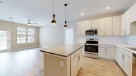 This single-floor, 2-bedroom, 2-bathroom residence offers a well-organized layout that balances comfort and modern design. The open-concept kitchen is a standout feature, showcasing crisp white cabinetry, subway tile backsplash, stainless steel appliances—including a range, microwave, and refrigerator—and a central island with a dark countertop accent, illuminated by a pair of stylish black-and-gold pendant lights. Warm-toned hardwood-style flooring runs throughout the main living areas, creating a cohesive and inviting atmosphere.

The living room extends naturally from the kitchen, benefiting from natural light through multiple windows. The primary bedroom is a comfortable retreat with plush carpeting, its own walk-in closet fitted with wire shelving, and an en-suite bathroom featuring a single vanity with ample drawer storage and a tiled tub-shower combination with brushed nickel fixtures. The second bedroom also features carpet flooring, a ceiling fan, and a window with outdoor views. A second full bathroom mirrors the quality finishes found throughout the home. Two closets provide generous storage, and a hallway connects all rooms efficiently for a functional, easy-to-navigate floor plan.
