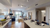 This thoughtfully designed single-floor residence showcases a seamless open-concept layout that connects the kitchen, dining, and living areas into one cohesive, light-filled space. Warm hardwood flooring flows throughout, complementing the clean, contemporary aesthetic. Track lighting in the main living area and recessed lighting elsewhere provide layered illumination across the space.

The kitchen is a standout feature, outfitted with rich walnut-toned lower cabinetry, crisp white upper cabinets, a classic subway tile backsplash, quartz countertops, and a full suite of stainless steel appliances. A kitchen island with seating extends into the dining area, creating a natural gathering point. The dining space transitions smoothly into the living room, which is anchored by a large sofa, curated artwork, and a set of sliding glass doors that open onto a private balcony overlooking a lush outdoor view.

The bedroom is a calm, well-proportioned retreat featuring soft neutral tones, bold artistic accents, and ample natural light from a large window. A dedicated media console and lounge chair add function and character to the room. The bathroom is clean and modern, featuring a wide vanity with an undermount sink, walnut cabinetry, a large mirror, and a shower-tub combination.