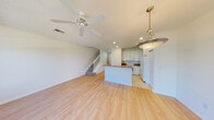 This two-story home offers a clean, functional layout with consistent finishes throughout. The entry hallway sets a welcoming tone with light hardwood flooring, crisp white walls, and panel doors leading to various rooms. The open-concept main living area flows seamlessly into the kitchen, where white cabinetry, granite countertops, a kitchen island, and a side-by-side refrigerator provide a practical and attractive workspace. A ceiling fan and pendant lighting add character to the combined living and dining space, which also features a staircase with a classic balustrade leading to the upper level. The bathrooms are finished with beige tile surrounds featuring decorative accent tiles, a soaking tub, a shower, and white vanity cabinetry. Upstairs, the landing opens to carpeted bedrooms, including a primary suite with an en-suite bathroom and a generous walk-in closet equipped with wire shelving and a natural light window. Additional bedrooms include standard closets with built-in rods. The home's consistent use of light tones, hardwood-style flooring on the main level, and plush carpet upstairs creates a cohesive and comfortable living environment throughout both floors.