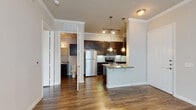 This single-floor unit offers a thoughtfully designed open-concept layout that seamlessly connects the kitchen and living areas. Rich hardwood-style flooring runs throughout the space, complemented by crisp crown molding that adds a refined architectural detail to every room.

The kitchen is a standout feature, boasting dark espresso cabinetry that extends to the ceiling for generous storage, granite countertops, and a full suite of stainless steel appliances including a refrigerator, electric range, and over-the-range microwave. A peninsula with seating overhang and elegant pendant lighting serves as both a functional workspace and a casual dining area. A subway tile backsplash adds a clean, modern touch.

The living and dining areas are open and generously proportioned, bathed in natural light from large windows fitted with blinds. The bedrooms continue the hardwood-style flooring and crown molding, each offering ample natural light and a neutral color palette that lends a calm, versatile ambiance.

The bathroom features a tiled soaking tub with shower combination, granite-topped vanity with dark cabinetry, and a large mirror. A convenient half bath is also accessible from the main living area. The overall design balances modern finishes with a warm, welcoming atmosphere throughout.