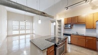 Located at 800 Lake Carolyn Pkwy in Irving, TX, this two-bedroom, two-bathroom residence offers a thoughtfully designed single-floor layout with a striking blend of industrial and modern aesthetics. The open-concept living and kitchen area immediately impresses with soaring ceilings, exposed ductwork, and a dramatic bank of floor-to-ceiling windows that flood the space with natural light and reflect beautifully off the polished stone-look floors. The kitchen is well-appointed with warm wood cabinetry, granite countertops, a central island with a built-in cooktop, stainless steel appliances including a refrigerator and dishwasher, a white tile backsplash, and built-in open shelving for added storage. Track lighting and pendant fixtures provide focused illumination throughout. Both bedrooms feature plush carpeting, ceiling fans, and generous windows with exterior views, creating comfortable and light-filled retreats. The primary bedroom includes a well-sized walk-in closet with wire shelving. The bathrooms are finished with granite-topped vanities and rich wood cabinetry. Additional conveniences include a dedicated laundry area, multiple closets, and hallways connecting the private and shared spaces seamlessly. The overall ambiance is contemporary and urban, ideal for those seeking a polished, functional living environment.