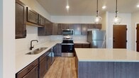 Located at 3700 42nd St S in Fargo, North Dakota, this single-floor residence offers a thoughtfully designed layout with a clean, contemporary aesthetic throughout. Warm neutral tones and a mix of hardwood-style and plush carpeted flooring create a cohesive and inviting atmosphere across all rooms.

The kitchen serves as a standout feature of the space, showcasing rich dark cabinetry, light quartz countertops, and a full suite of stainless steel appliances including a refrigerator, electric range, and built-in microwave. A central island with pendant lighting adds both function and style, while recessed lighting and a matte black sink fixture complete the modern look.

The living area is bright and open, with a sliding glass door leading to a private outdoor deck, allowing natural light to fill the room. Multiple bedrooms offer comfortable retreats, each with plush carpeting, natural light from well-positioned windows, and generous closet space. One bedroom features a ceiling fan, while another includes a wall-mounted air conditioning unit for added climate control.

The bathrooms are finished with the same dark cabinetry and quartz countertops found in the kitchen, complemented by hardwood-style flooring and clean white fixtures. A walk-in closet with wire shelving provides ample storage directly off one of the bathrooms, enhancing the unit's practical appeal.