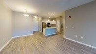 This single-floor residence offers a thoughtfully designed open-concept layout that seamlessly connects the living area to the kitchen. The living room features durable wood-look plank flooring, a ceiling fan, and a window with a view to the outdoors, creating a bright and welcoming atmosphere. A pendant light fixture above the dining area adds a stylish accent to the space.

The kitchen is a standout feature, equipped with crisp white cabinetry, granite-look countertops, and a full suite of stainless steel appliances including a refrigerator, range, and over-the-range microwave. A kitchen island with a built-in sink provides additional workspace and serves as a natural focal point of the open floor plan. Wood-look plank flooring continues throughout the kitchen and main living areas.

The bedrooms are carpeted for comfort and include ample natural light from windows fitted with blinds. One bedroom features a ceiling fan and dual windows, while another includes a double-door closet. Both bathrooms are finished with white vanity cabinetry, granite-look countertops, and wood-look flooring. The primary bathroom includes a walk-in glass-door shower, while the secondary bathroom offers a full shower-tub combination. Neutral warm-gray wall tones carry throughout the entire residence, contributing to a cohesive and modern aesthetic.