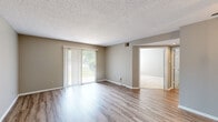 This single-floor, 1-bedroom, 2-bathroom unit offers a thoughtfully organized layout that maximizes functionality throughout. The combined living and dining area serves as the heart of the home, featuring warm-toned hardwood-style flooring, neutral taupe walls, and a textured ceiling. A large sliding glass door with vertical blinds fills the space with natural light and provides access to the outdoors. The kitchen is designed for efficiency, featuring rich dark-wood cabinetry, a mosaic tile backsplash, granite-style countertops, a double-basin sink, and black appliances including a refrigerator, range, and dishwasher. A convenient pass-through counter connects the kitchen to the main living area. The bedroom is carpeted for comfort, offering a tranquil retreat with a natural light source via a window with blinds and direct access to a generously sized walk-in closet outfitted with wire shelving and built-in storage units. A second closet provides additional storage. Both bathrooms feature dark-wood vanities with white countertops, large mirrors, and hardwood-style flooring. The den offers versatile additional space with matching hardwood-style flooring. An in-unit laundry area and a connecting hallway complete the practical and cohesive floor plan.
