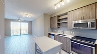 Located at Port Royale Drive in Fort Lauderdale, this 3-bedroom, 2-bathroom apartment offers a contemporary living experience across a single, well-organized floor. The open-concept kitchen is outfitted with wood-grain cabinetry, open shelving, a subway tile backsplash, white quartz countertops, a stainless steel sink, and a full suite of stainless steel appliances including a gas range, dishwasher, and built-in microwave. A freestanding kitchen island provides additional prep and dining space. Light-toned tile flooring that mimics hardwood runs throughout the entire unit, creating a cohesive and clean aesthetic. The spacious living area benefits from abundant natural light through large sliding glass doors that open to a balcony, complemented by a ceiling fan overhead. The bedrooms are generously proportioned, with large windows that frame scenic views of the marina and surrounding greenery. The primary bedroom includes direct access to an en-suite bathroom featuring a wood-tone vanity with quartz countertops and a large glass-enclosed walk-in shower with white subway tile surround and chrome fixtures. The second bathroom mirrors the same refined finishes. Throughout the unit, neutral warm-gray walls and bright white trim contribute to a clean, modern ambiance ideal for South Florida living.
