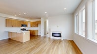 Located at 4237 Cameo Ln in Bellingham, Washington, this contemporary 3-floor home offers a well-designed layout with modern finishes throughout. The ground floor includes a spacious attached garage with an automatic opener and transom windows that allow natural light into the space. The main living level showcases an open-concept floor plan with light wood flooring that flows seamlessly from the kitchen through the living area. The kitchen is appointed with warm wood cabinetry, a large island featuring a white quartz countertop and undermount sink, stainless steel appliances, and recessed lighting. The adjacent living area centers around a sleek, modern fireplace framed by clean white walls. A sliding glass door opens to a private balcony, extending the living space outdoors. The upper floor houses the bedrooms, each carpeted and filled with natural light from well-placed windows. Bedrooms are equipped with individual wall-mounted mini-split units for personalized climate control. A bright, clean bathroom with wood-look flooring and white fixtures completes the upper level. The exterior features a contemporary mix of siding colors and an additional covered balcony, contributing to the home's modern curb appeal.