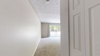 Located at 6910 Brooklawn Dr in Louisville, Kentucky, this one-bedroom, one-bathroom unit offers a well-organized single-floor layout designed for comfortable everyday living. The living room is generously proportioned, featuring plush carpeting, neutral beige walls, a textured ceiling, and a large sliding glass door framed by white curtains that fills the space with natural light and provides direct outdoor access and views of surrounding greenery. The open sightline from the living area connects seamlessly to the galley-style kitchen, which is outfitted with dark espresso cabinetry, granite-look countertops, wood-look vinyl flooring, and white appliances including a refrigerator and range. The bedroom is a comfortable, well-sized retreat with soft carpeting, a textured ceiling, a window overlooking outdoor greenery, and a double-door closet providing ample storage. The bathroom features a full tub-shower combination with floor-to-ceiling warm-toned tile surround and chrome fixtures, offering a clean and classic look. Throughout the unit, consistent neutral tones, carpet in living and sleeping areas, and practical finishes create a cohesive and functional living environment. A dedicated closet adds additional storage convenience to the layout.