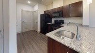 Located at 409 E Sheridan Ave in the Steelyard community of Oklahoma City, this single-floor unit offers a clean, modern interior designed for comfortable everyday living. The open-concept layout connects the kitchen and living areas seamlessly, with dark wood-style vinyl plank flooring running throughout the main living spaces, creating a cohesive and contemporary aesthetic.

The kitchen is well-appointed with rich dark cabinetry, granite countertops, a stainless steel undermount sink, and black appliances including a refrigerator, electric range, and over-the-range microwave. A peninsula provides additional prep space and helps define the kitchen from the adjacent dining and living areas. Pendant lighting adds a polished finishing touch overhead.

The dining area benefits from direct natural light through a large window fitted with white horizontal blinds, while a ceiling fan provides comfortable air circulation. The bedroom continues the neutral palette with soft carpeting underfoot, dual windows for natural light, and its own ceiling fan.

The bathroom features dark cabinetry with brushed nickel hardware, granite countertops, a framed mirror, and wood-style flooring that complements the rest of the unit. A separate water closet houses the toilet and a full tub-shower combination. Throughout, crisp white walls, clean trim, and recessed lighting contribute to a bright, move-in-ready atmosphere.