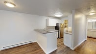 Located at 7024 North Colton Street in Spokane, WA, this single-floor unit offers a thoughtfully updated interior with a clean, modern aesthetic throughout. Rich wood-look flooring flows seamlessly across the open-concept living and kitchen areas, complemented by crisp white walls and textured ceilings that add depth to the space.

The kitchen is a standout feature, centered around a peninsula with a built-in sink and gray countertops that provide both prep space and casual seating. White upper cabinetry pairs with a mosaic tile backsplash, while stainless steel appliances — including a refrigerator and electric range with an overhead ventilation hood — complete the functional layout. Baseboard heating units are positioned throughout for consistent warmth.

The spacious living area benefits from abundant natural light courtesy of a sliding glass door that opens to the outdoors, and a wall-mounted AC unit ensures year-round comfort. The bedroom wing includes a generous room with direct access to a walk-in closet and an attached bathroom. Two bathrooms are present in the unit; both feature wood-look flooring, tub/shower combinations, and updated vanities with gray countertops and mosaic tile accents. A dedicated laundry area houses a full-size side-by-side washer and dryer with built-in shelving above for additional storage.