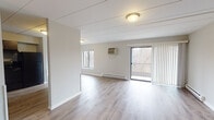 Located at 11 Victor Dr in Hobart, Indiana, this single-floor unit offers a clean, functional layout designed for comfortable everyday living. The spacious living area is finished with light wood-tone laminate flooring and features a sliding glass door flanked by vertical blinds that opens to a private balcony with wooded views, allowing natural light to flow freely throughout the space. A wall-mounted air conditioning unit and baseboard heating provide year-round climate control.

The kitchen is well-appointed with rich, dark cabinetry, stone-look countertops, a stainless steel sink, and a black electric range with an overhead exhaust hood, offering both style and practicality. An additional room with matching laminate flooring provides flexible living or dining space with convenient hallway access.

The bedrooms are carpeted for comfort and each include wall-mounted AC units, baseboard heating, and ample natural light from large windows. One bedroom features a roomy closet with a hanging rod, providing solid storage capacity.

The bathrooms are finished with wood-look tile flooring and include full tub-shower combinations with white surrounds and chrome fixtures, presenting a clean and updated aesthetic throughout. The overall palette of neutral grays and whites gives the entire unit a bright, move-in-ready feel.