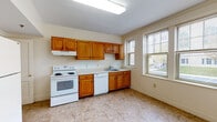 Located at 4 Nazing Court in Boston's Dorchester neighborhood, this single-floor unit offers a well-organized layout with a practical design throughout. The kitchen is a central feature of the space, equipped with warm honey-toned wood cabinetry extending both above and below the countertops, white appliances including an electric range and dishwasher, a stainless steel sink, and tile flooring. A dedicated pantry or storage closet is accessible directly from the kitchen, adding valuable organizational space. Natural light enters through double-hung windows fitted with blinds, offering views of the surrounding neighborhood.

The living areas and bedrooms feature richly polished hardwood floors that carry a warm, glossy tone throughout. Several rooms include classic wall paneling details and large windows that invite abundant natural light. One room features a triple-window bay, while others offer views of neighboring greenery. A closet is present in at least one of the bedrooms, providing built-in storage.

The bathroom includes a full tub and shower combination with a curtain rod, a wood-cabinet vanity with a sink and mirror, tile flooring, and safety grab bars installed near the tub. The overall ambiance of the unit is clean, neutral, and move-in ready.