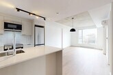 Located at 2198 Boulevard De Maisonneuve Est in Montréal, this thoughtfully designed one-bedroom, one-bathroom unit offers a clean, contemporary aesthetic throughout. The open-concept living and kitchen area serves as the heart of the unit, anchored by a sleek white quartz island with an integrated sink. The kitchen is well-appointed with flat-panel cabinetry, white subway tile backsplash, stainless steel appliances including a refrigerator, stove, and built-in microwave, complemented by directional track lighting overhead. Light oak hardwood flooring runs throughout the main living areas, adding warmth against the crisp white walls. A defining architectural feature is the exposed concrete ceiling, which lends an industrial character to the space. The living area is generously lit by large windows that frame views of the surrounding Montréal streetscape. The bedroom continues the same hardwood flooring and exposed concrete ceiling, with a sizable window providing natural light and urban views. The bathroom is finished with large-format neutral tiles, a wall-mounted floating vanity, a glass-enclosed shower, and a stacked in-unit washer and dryer — a highly practical inclusion. Overall, the unit presents a modern, minimalist character well-suited to urban living in the heart of Montréal.