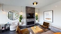 This thoughtfully designed single-floor amenity lounge combines modern aesthetics with inviting functionality. The space is anchored by a striking living area centered around a floor-to-ceiling dark tile fireplace surround, complete with a wall-mounted television and flanked by lush fiddle-leaf fig plants. Warm copper pendant lights and a circular statement mirror add character, while plush seating in earth tones — including velvet accent chairs and a natural wood coffee table — creates an atmosphere that is both stylish and comfortable. Dark hardwood-style flooring flows throughout, grounding the open layout with sophistication.

Adjacent to the lounge, a dining area makes an immediate impression with a large, locally inspired illustrated mural that serves as a vibrant focal point. An oval live-edge wood table surrounded by sleek white chairs sits beneath a trio of copper pendant lights, while floor-to-ceiling black-framed glass doors open to an outdoor balcony, flooding the room with natural light and providing views of the surrounding neighborhood.

A dedicated wet bar area rounds out the space, featuring warm taupe-toned glazed tile cladding the full wall, a stainless steel sink, a smooth quartz countertop, and white cabinetry. Together, these distinct zones create a versatile, well-appointed gathering space suited for both relaxed socializing and more formal meetings.