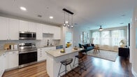 Located at 3050 Station Square in Kissimmee, Florida, this single-floor residence offers a thoughtfully designed open-concept layout with modern finishes throughout. The kitchen is a standout feature, showcasing crisp white shaker cabinetry reaching to the ceiling, stainless steel appliances, a marble-style tile backsplash, and quartz countertops. A central island with seating for two serves as both a prep space and casual dining area, illuminated by a trio of globe pendant lights that add a contemporary touch. Rich hardwood-style flooring flows seamlessly from the kitchen into the living area, where natural light pours in through large windows dressed in sheer curtains. The living room provides a welcoming retreat with a ceiling fan and ample wall space for décor. Two well-proportioned bedrooms are finished with plush carpeting, ceiling fans, and windows that invite natural light and outdoor views. The bathrooms are elegantly appointed — one features a wide vanity with an LED-backlit mirror and a tub/shower combo, while the other includes a glass-enclosed walk-in shower with marble-style tile surround and wood-look flooring. The overall ambiance is clean, contemporary, and comfortable, making this Kissimmee residence a refined living space.