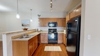 This single-floor residence offers a thoughtfully designed layout that balances functionality and comfort. The kitchen is a standout feature, equipped with warm honey-toned wood cabinetry, granite-look countertops, a classic white tile backsplash, and a full suite of black appliances including a range, over-the-range microwave, and refrigerator. Track lighting overhead and a stylish pendant light illuminate the space, while rich hardwood flooring adds warmth. A breakfast bar with an overhang connects the kitchen to the adjacent living and dining area, creating an open, inviting flow ideal for everyday living and entertaining.

The living area is generously proportioned, featuring the same hardwood flooring, a ceiling fan with light fixture, and access to natural light through a windowed door. Neutral-toned walls provide a versatile backdrop throughout the home.

The bedrooms offer plush carpeting, soft neutral walls, and windows fitted with white horizontal blinds that allow for natural light and greenery views. The bathrooms are clean and functional, each featuring a wood-toned vanity, white countertop, large mirror, and a tub/shower combination. The consistent use of warm wood tones and neutral finishes gives the entire residence a cohesive and comfortable aesthetic.