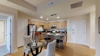 Located at 659 Rice Boulevard in Exton, Pennsylvania, this single-floor residence offers a thoughtfully designed living space with modern finishes throughout. The open-concept kitchen is a standout feature, showcasing warm maple cabinetry that extends to the ceiling, dark granite countertops, and a full suite of stainless steel appliances including a refrigerator, microwave, and dishwasher. A central kitchen island with bar seating provides a casual dining option and serves as the natural hub of the space. Recessed lighting and a stylish pendant fixture illuminate the kitchen, enhancing its contemporary aesthetic. Light hardwood flooring flows seamlessly through the area, adding warmth and continuity. The adjacent dining area accommodates a round glass-top table with upholstered seating, creating an elegant yet approachable atmosphere for meals and gatherings. Clean white walls and neutral tones throughout contribute to a bright, airy ambiance. The layout is practical and efficient, with interior doors providing access to additional areas of the residence. A modern keypad entry system is visible near the entrance, reflecting the thoughtful integration of convenience and security in this well-appointed home.