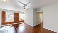 Located in the heart of Hollywood at 6500 Yucca St, Los Angeles, this single-floor unit combines industrial character with modern updates for a distinctive living experience. The main living area is generously proportioned, featuring warm light hardwood flooring throughout, crisp white walls, and a ceiling fan that adds both style and functionality. A standout feature of the space is the exposed red brick wall, which adds rich texture and industrial charm, framed by large windows that invite natural light and offer views of the surrounding Hollywood neighborhood, including glimpses of palm trees and nearby architecture. The open layout flows seamlessly from the living area into the kitchen, which is accessed through a dedicated opening. The kitchen is outfitted with white shaker-style cabinetry, light countertops, a stainless steel sink with a modern faucet, and tile flooring — offering a clean, contemporary aesthetic. The bathroom is finished with a tiled tub and shower combination, maintaining the unit's clean and functional design language. Overhead HVAC venting is integrated into the ceiling alongside flush-mount lighting, ensuring year-round comfort. The overall ambiance is bright, airy, and urban, blending classic architectural details with updated finishes throughout.