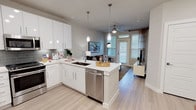 This single-story residence offers a well-designed open-concept layout that seamlessly connects the kitchen, dining, and living areas. The kitchen is a standout feature, showcasing high-gloss white cabinetry, quartz countertops, a grey subway tile backsplash, and a full suite of stainless steel appliances, including a French door refrigerator, range, microwave, and dishwasher. A peninsula with pendant lighting serves as both a functional workspace and a casual dining area, while light wood-style flooring runs throughout the main living spaces, contributing to a clean, contemporary aesthetic.

The living area benefits from natural light through multiple windows dressed with blinds and curtains, and a ceiling fan overhead adds comfort. The bedroom is a calm, well-lit retreat with a ceiling fan, large windows allowing ample natural light, and direct access to a walk-in closet. The en-suite bathroom features a tub and shower combination accented by marble-style tile, chrome fixtures, and a crisp white color palette. Overall, the space presents a cohesive modern design with neutral tones and quality finishes throughout.