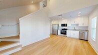 Located at 1545 Payne St in Tallahassee, Florida, this two-bedroom, two-bathroom two-story home offers a well-designed layout spread across two floors. The main floor hosts the open-concept living, dining, and kitchen area, where vaulted ceilings soar overhead and a ceiling fan adds a practical touch. Large windows allow natural light to fill the space, complementing the light hardwood flooring that runs throughout the home. The kitchen is outfitted with crisp white shaker-style cabinetry, granite-look countertops, and a full suite of stainless steel appliances including a refrigerator, range, microwave, and dishwasher — all illuminated by recessed lighting. A dedicated laundry area and multiple closets add functional storage. The main floor bathroom features a walk-in shower, white vanity with granite countertop, and matching hardwood flooring. Upstairs, the second floor features a charming bedroom with a sloped ceiling, built-in storage access, and a secondary bathroom with a pedestal sink. The primary bedroom on the main level is generously sized with a ceiling fan and ample natural light. Clean white walls and consistent finishes give the entire home a bright, modern, and cohesive aesthetic.