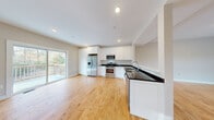 Located at 5 Marwari Ln. in Rochester, New Hampshire, this two-floor residence offers a clean, modern aesthetic with thoughtfully designed living spaces across both levels. Warm-toned hardwood flooring flows consistently throughout, creating a cohesive and inviting atmosphere from room to room.

The main level centers around an open-concept kitchen and living area, designed for both functionality and comfort. The kitchen is outfitted with crisp white shaker cabinetry, dark granite countertops, and a full suite of stainless steel appliances including a gas range, over-the-range microwave, French door refrigerator, and dishwasher. A peninsula with a built-in sink adds additional prep space and a natural gathering point. A sliding glass door opens to an outdoor deck, allowing natural light to fill the space and providing views of the surrounding wooded landscape.

The living area is generously proportioned, with recessed lighting and a central staircase connecting both floors. The upper level features multiple well-sized bedrooms, each with large windows that frame natural views and fill the rooms with daylight. A walk-in closet with wire shelving provides practical storage. The bathroom includes a walk-in shower, a white vanity with dark countertop, tile flooring, and a window for natural light. Throughout the home, neutral wall tones and clean white trim contribute to a fresh, move-in-ready feel.