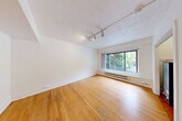 Located in Seattle's vibrant Belltown neighborhood, this efficiently designed single-floor unit at 2205 2nd Ave offers a well-organized layout that includes a living room, dining room, kitchen, bathroom, closet, and entrance. Warm hardwood floors run throughout the main living areas, lending a classic and inviting feel to the space. The living room is bright and open, featuring track lighting and a large picture window that frames leafy outdoor views and fills the room with natural light. A baseboard heating system runs beneath the windows, ensuring year-round comfort. The kitchen is thoughtfully appointed with white cabinetry featuring glass-front upper doors, white subway tile backsplash, light countertops, and a stainless steel sink. A sizable window over the counter brings in natural light and greenery views, while a pendant light adds a charming finishing touch. The bathroom includes a sleek wall-mounted sink with a brass-framed console stand, a vanity mirror, and open shelving, presenting a clean and functional aesthetic. A dedicated closet with built-in shelving provides practical storage. Throughout the unit, crisp white walls complement the warm wood floors, creating a clean, airy ambiance well-suited to urban living in the heart of Seattle.