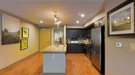 This single-floor residence offers a thoughtfully designed open-concept layout that seamlessly blends style and functionality. The kitchen serves as the centerpiece of the space, showcasing rich dark cabinetry that contrasts beautifully with light granite countertops. A central kitchen island with an undermount sink provides additional workspace and casual dining potential, while elegant pendant lighting hangs above, adding a warm, inviting atmosphere. Recessed lighting throughout ensures the space is well-lit and welcoming.

The kitchen is equipped with stainless steel appliances, including a full-size refrigerator and a range, complemented by a classic tile backsplash that adds a clean, polished finish. Warm hardwood flooring flows continuously throughout the space, enhancing its cohesive and modern aesthetic.

A framed piece of wall art near the entryway adds a personal touch, while the natural wood-tone front door provides a welcoming transition into the home. The open layout allows for excellent sightlines across the living areas, making the space feel expansive and airy. Overall, this residence combines contemporary design elements with practical features, creating a comfortable and visually appealing living environment.