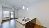 This single-floor unit features a thoughtfully designed open-concept layout that seamlessly connects the kitchen and living areas. The kitchen serves as a focal point, centered around a large island with a double stainless steel sink and granite countertop. Dark espresso cabinetry extends to the ceiling, providing generous storage, while stainless steel appliances—including a refrigerator, microwave, and range—complete the space. A mosaic tile backsplash adds a subtle decorative touch behind the cooking area.

Pendant lighting hangs above the kitchen island, complementing the recessed lighting throughout. The living area benefits from warm hardwood-style flooring that extends throughout the unit, a ceiling fan, and a glass door that invites natural light and provides outdoor views of the surrounding area.

The bedrooms are well-proportioned, each equipped with ceiling fans and large windows fitted with blinds, allowing for controlled natural light. One bedroom features a glass exterior door, adding additional brightness and outdoor access.

The bathroom maintains the cohesive design aesthetic with dark cabinetry, a granite vanity countertop, a large mirror, overhead storage, and tile-accented walls near the shower area. Wood-style flooring continues into the bathroom, tying the overall design together cohesively.
