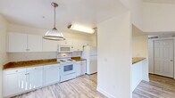 Located at 1711 W Henderson Ave in Porterville, CA, this well-appointed one-bedroom, one-bathroom residence offers a thoughtfully organized single-floor layout. The open-concept kitchen and dining area is a standout feature, showcasing white shaker-style cabinetry, rich granite-look countertops, white appliances including a range, built-in microwave, and refrigerator, plus a stylish pendant light overhead. Light wood-look flooring flows throughout the kitchen, dining, and living areas, creating a bright and cohesive feel. The spacious living room features vaulted ceilings, a ceiling fan, and a sliding glass door that opens onto a private balcony with outdoor views. The bedroom is carpeted for comfort, includes a ceiling fan, and is served by three closets for ample storage. The full bathroom mirrors the kitchen's design aesthetic with granite-look counters, white cabinetry, and a tub/shower combination. Additional conveniences include a dedicated laundry area, a pantry, a utility room, and a hallway connecting the spaces efficiently. The unit's clean, neutral palette and consistent finishes create a cohesive and move-in-ready living environment.