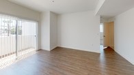 This single-floor unit presents a clean, modern aesthetic throughout its thoughtfully designed layout. The open living area is finished with warm hardwood-style flooring and receives natural light through a large sliding glass door fitted with vertical blinds, creating a bright and welcoming atmosphere. An adjacent room with matching flooring offers additional flexible living space, complete with recessed track lighting and built-in ceiling ventilation.

The kitchen is well-equipped with light wood cabinetry, dark countertops, stainless steel appliances including a gas range, over-the-range microwave, and a decorative mosaic tile backsplash that adds visual interest to the space.

Multiple bedrooms feature soft, neutral-toned carpeting and windows fitted with horizontal blinds. Views from the bedrooms vary, with some overlooking neighboring urban structures and others offering glimpses of palm trees, suggesting a warm climate setting.

The bathrooms maintain a consistent modern design, featuring light wood vanity cabinetry with dark countertops, tile flooring, large mirrors, and full soaking tubs with tiled surround and overhead shower fixtures. The overall palette throughout the unit is neutral and understated, contributing to a calm, cohesive ambiance.