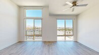 This thoughtfully designed single-floor unit offers a bright, contemporary living experience across a compact yet efficient footprint. The open-concept kitchen and living area serves as the heart of the space, featuring light wood-toned flooring throughout that enhances the clean, modern aesthetic. The kitchen is outfitted with white shaker-style cabinetry extending to the ceiling with frosted glass upper panels, stone-finish countertops, a large central island with matching countertop, and a full suite of stainless steel appliances including a French door refrigerator, double wall oven, built-in microwave, dishwasher, and a gas cooktop beneath a sleek stainless steel range hood. A white subway tile backsplash completes the polished look. The living area benefits from floor-to-ceiling sliding glass doors and a stacked transom window above, flooding the space with natural light and offering sweeping views of the surrounding cityscape and distant mountains. A ceiling fan adds functional comfort overhead. A stylish barn door leads to an additional room, maintaining the modern design language. The bathroom features a walk-in shower enclosed by a frameless glass door, finished with elegant marble-look tile surround. This unit combines upscale finishes with an airy, light-filled atmosphere.