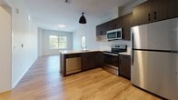 Located in Bloomfield, CT, this single-floor residence offers a thoughtfully designed layout with modern finishes throughout. The open-concept kitchen and living area serves as the heart of the home, featuring warm wood-tone LVP flooring that flows seamlessly through the main living spaces. The kitchen is well-appointed with dark espresso cabinetry, a subway tile backsplash, stainless steel appliances including a refrigerator, electric range, over-the-range microwave, and dishwasher, along with a peninsula that provides additional counter space and separates the kitchen from the living area. Large windows allow generous natural light to fill the living space, offering views of the surrounding greenery. The bedrooms are comfortably sized and finished with plush wall-to-wall carpeting, neutral walls, and ample closet space. One bedroom features a wide window with tree-lined outdoor views, enhancing the sense of openness. The bathroom is finished with wood-look LVP flooring, a white vanity with black hardware, and includes an accessibility grab bar, reflecting a practical and inclusive design. Overall, the unit presents a clean, contemporary aesthetic with a neutral palette, making it a versatile and functional living space.