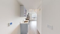 Located in Seattle's Capitol Hill neighborhood, this studio offers a thoughtfully designed layout that maximizes every inch of its compact footprint. The space is finished with light wood-tone flooring throughout, crisp white walls, and recessed lighting, creating a clean, contemporary aesthetic.

The galley-style kitchen is well-equipped with stainless steel appliances, including a full-size refrigerator, electric range, and over-the-range microwave. Gray lower and upper cabinetry, open shelving, and a single-basin sink with a modern faucet provide functional storage and prep space.

The main living area benefits from a large picture window that frames notable city and skyline views, flooding the room with natural light. A built-in Murphy bed cabinet offers a space-saving sleep solution while keeping the living area open and versatile. An additional closet alcove provides supplementary storage.

The bathroom maintains the studio's clean, minimal design with light tile flooring, a toilet, and a shower, all finished in a bright white palette. Overall, this studio presents an efficient, modern urban living option with quality finishes and an elevated city perspective in one of Seattle's most walkable neighborhoods.